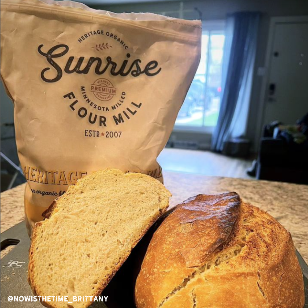 Loaf of bread with 'Sunrise Flour Mill' bag in a cozy kitchen setting.