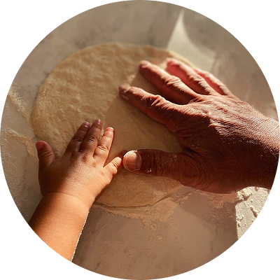 Child and adult hand pressing dough on a floured surface.